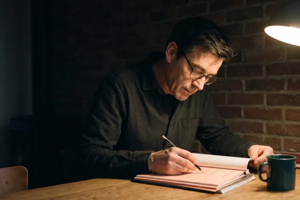 Een man leest 's avonds een dik gedrukt rapport aan een bureau en zet er met potlood een aantekening bij